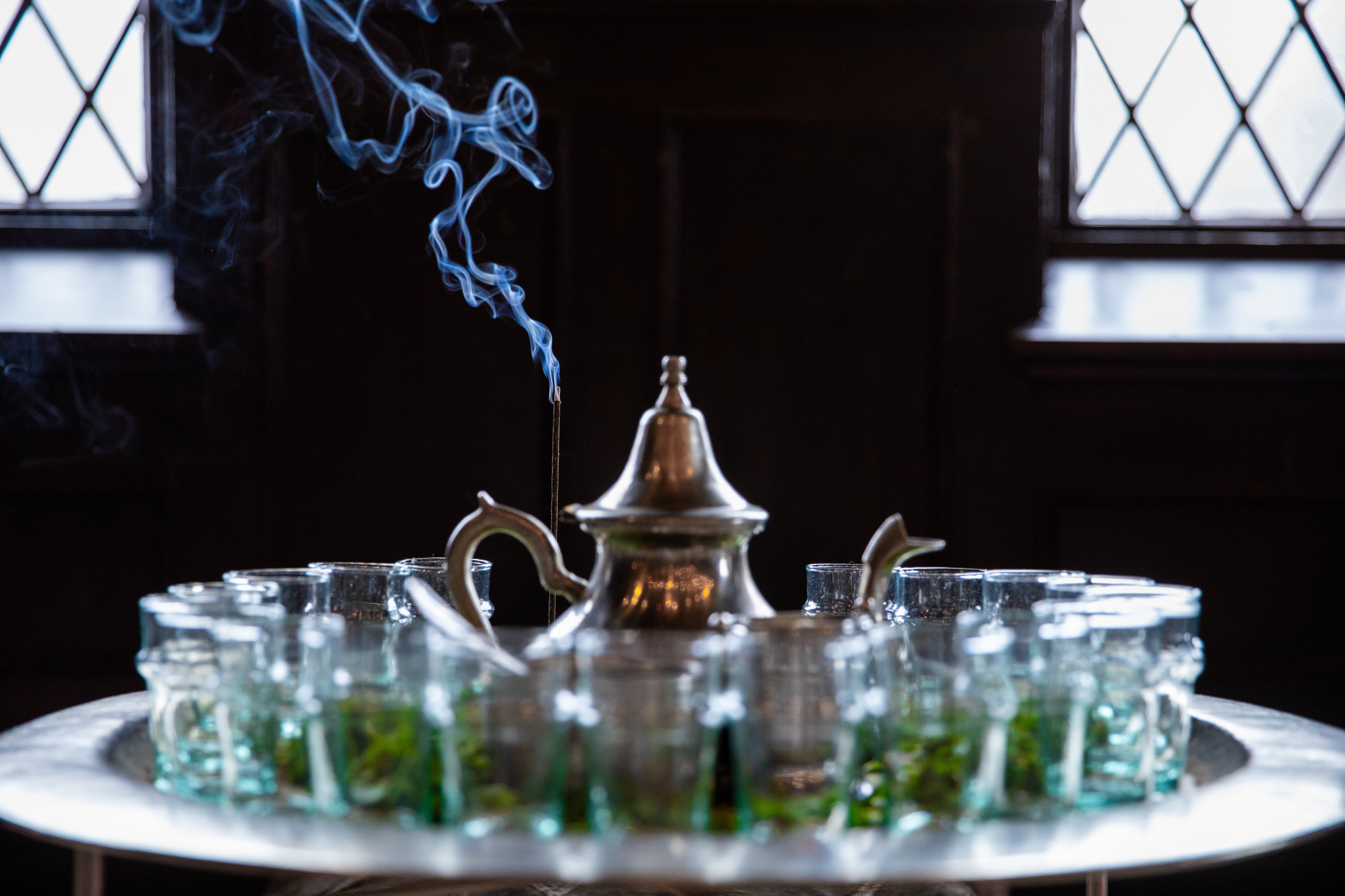 an ornate silver tea pot surrounded by beldi glasses with steam coming from an incense burner