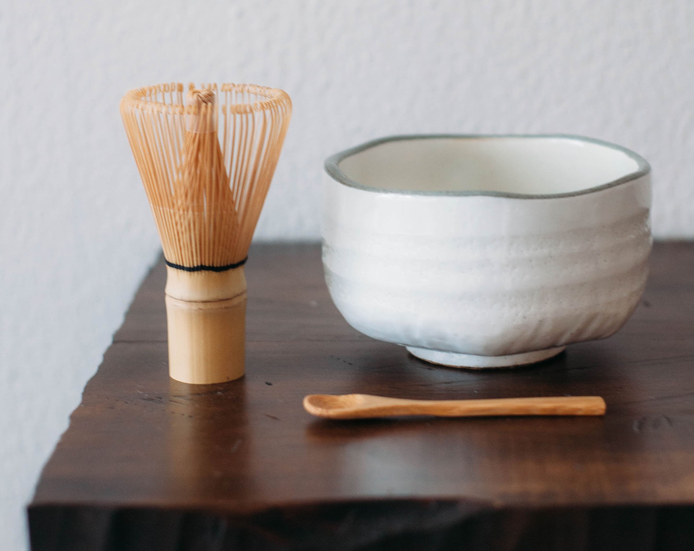 Firepot matcha accessories: a bamboo whisk, a white bowl, and a wooden spoon