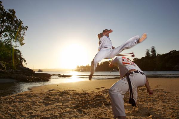 Men practicing Capoeira on the beach at sunset