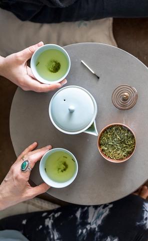 a display of green loose leaf tea, a white tea pot, incense burner, and two white cups of hot green tea