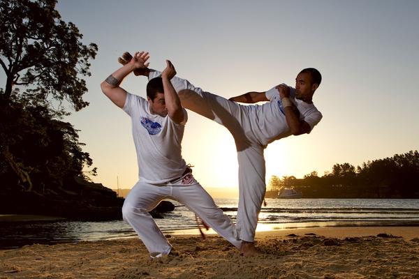 Men practicing Capoeira on the beach at sunset